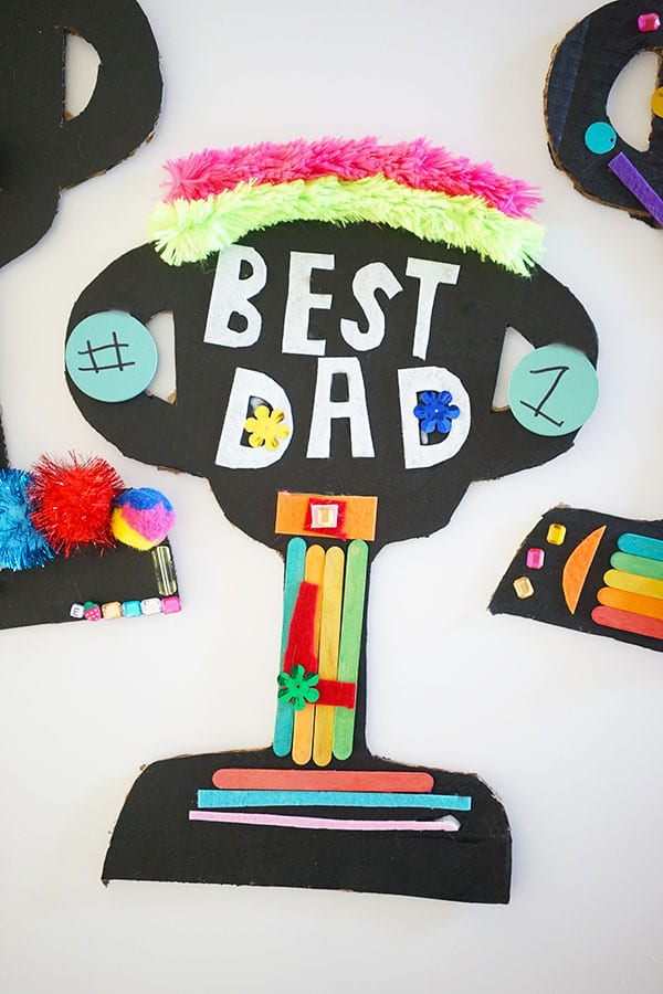 Trophy cut out decorated with letters that say Best Dad, popsicle sticks, and other embellishments. 