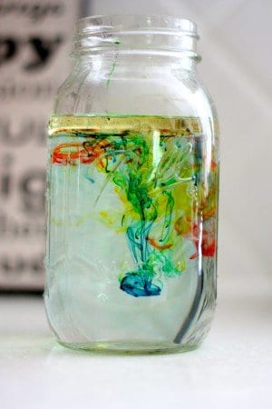 Water-filled mason jar with drops of food coloring sinking.