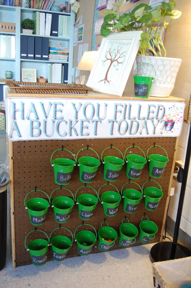 Green tin mini buckets hang from a pegboard with sign "Have you filled a Bucket Today?"
