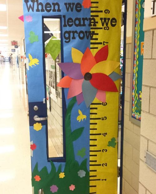 Door decorated with a large paper ruler and colorful flowers. Text reads When we learn we grow.
