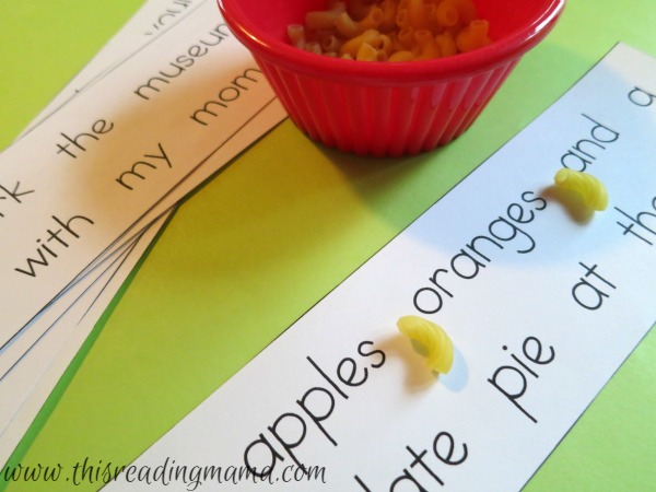 On a green table, sentence strips with elbow macaroni being used as commas as an example of grammar games