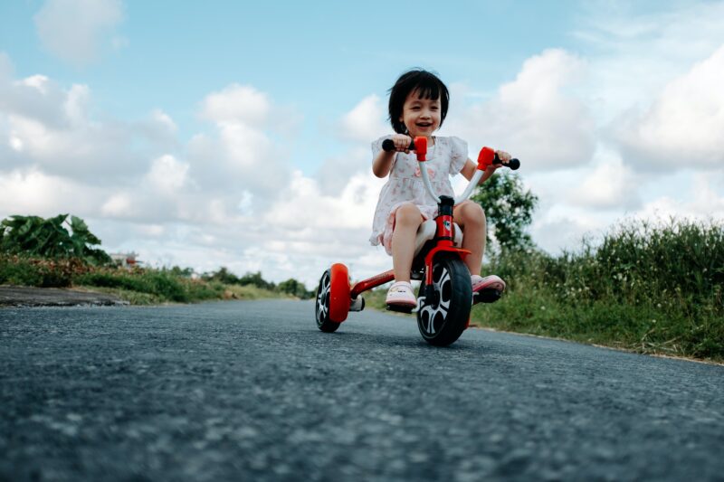 Preschool girl riding a tricycle outside, as an example of gross motor skills.