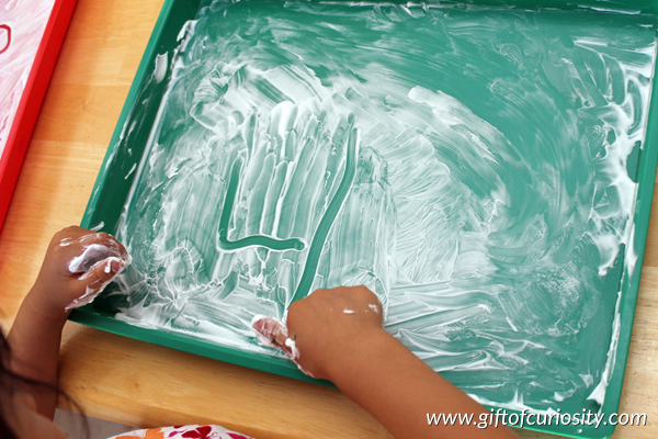 child writing in shaving cream on a try for a preschool activity