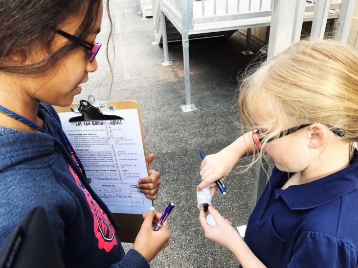 Two students finding a geocache, one holding a clipboard while the other opens a container