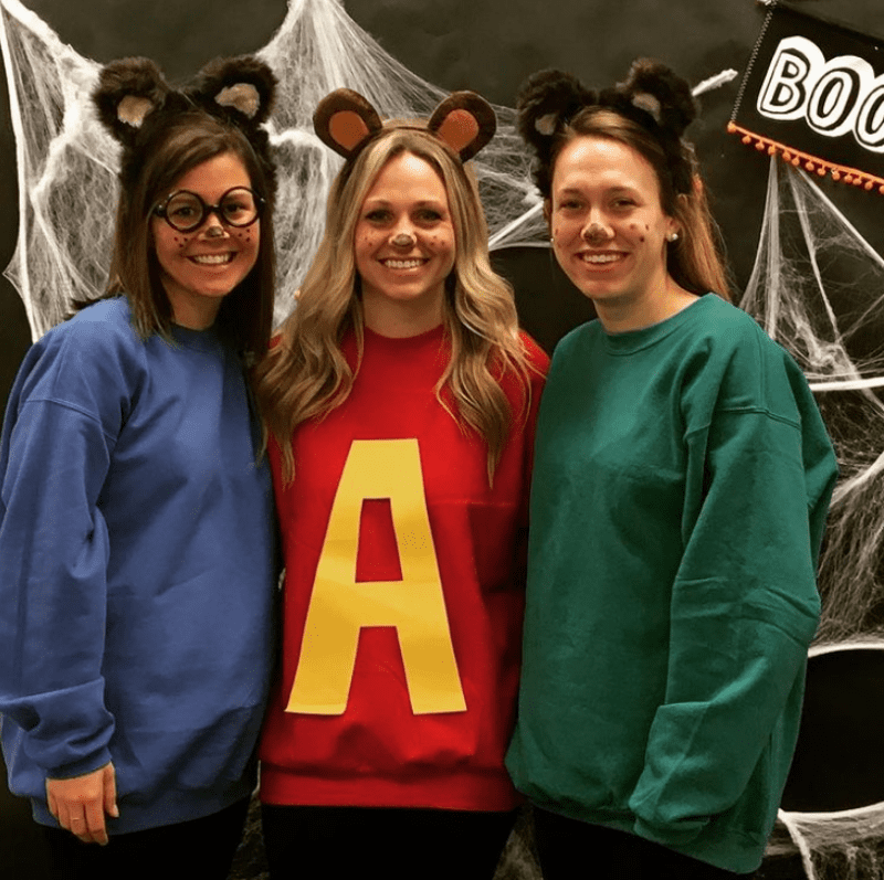 Three women are dressed up as Alvin, Simon, and Theodore in a blue sweatshirt, a red sweatshirt with a yellow A, and a green sweatshirt.