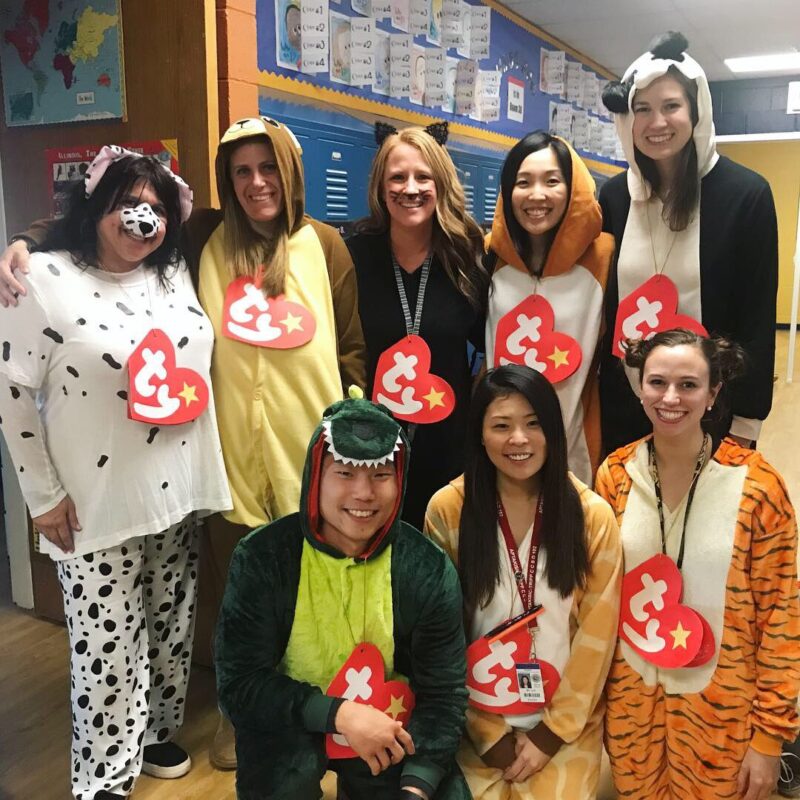 Eight teachers are in a group photos dressed as different animal beanie babies. They all have large tags around their necks with the trademark TY on them.
