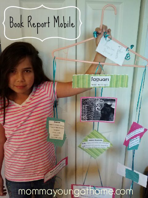 A girl stands next to a book report mobile made from a wire hanger and index cards as an example of creative book report ideas
