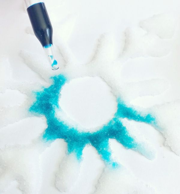 Blue liquid being dropped onto a snowflake shape made of salt