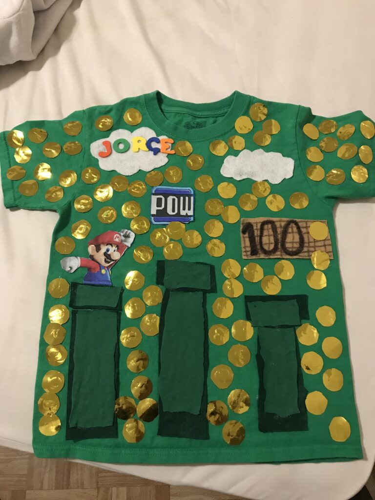 A green shirt features Mario from the Super Mario Brothers video game. 100 gold coins are all over the shirt.