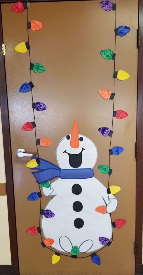 Winter classroom doors include this one that shows a snowman swinging on a string of colored Christmas lights.