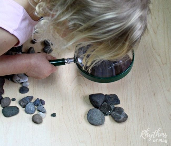 Child peering at a pile of rocks through a magnifying glass