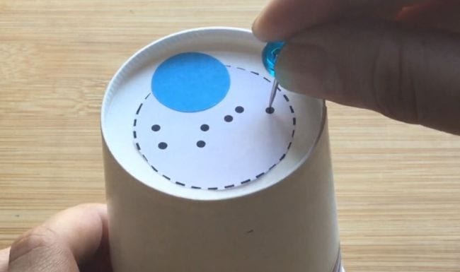 Science student poking holes in the bottom of a paper cup in the shape of a constellation