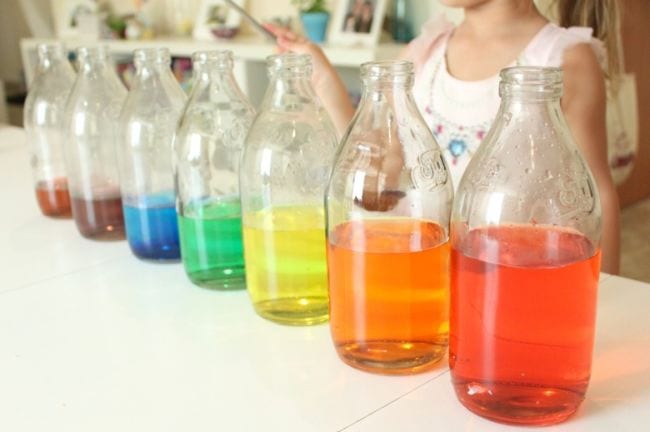 A series of bottles filled with different levels of different colored liquids to form a rainbow