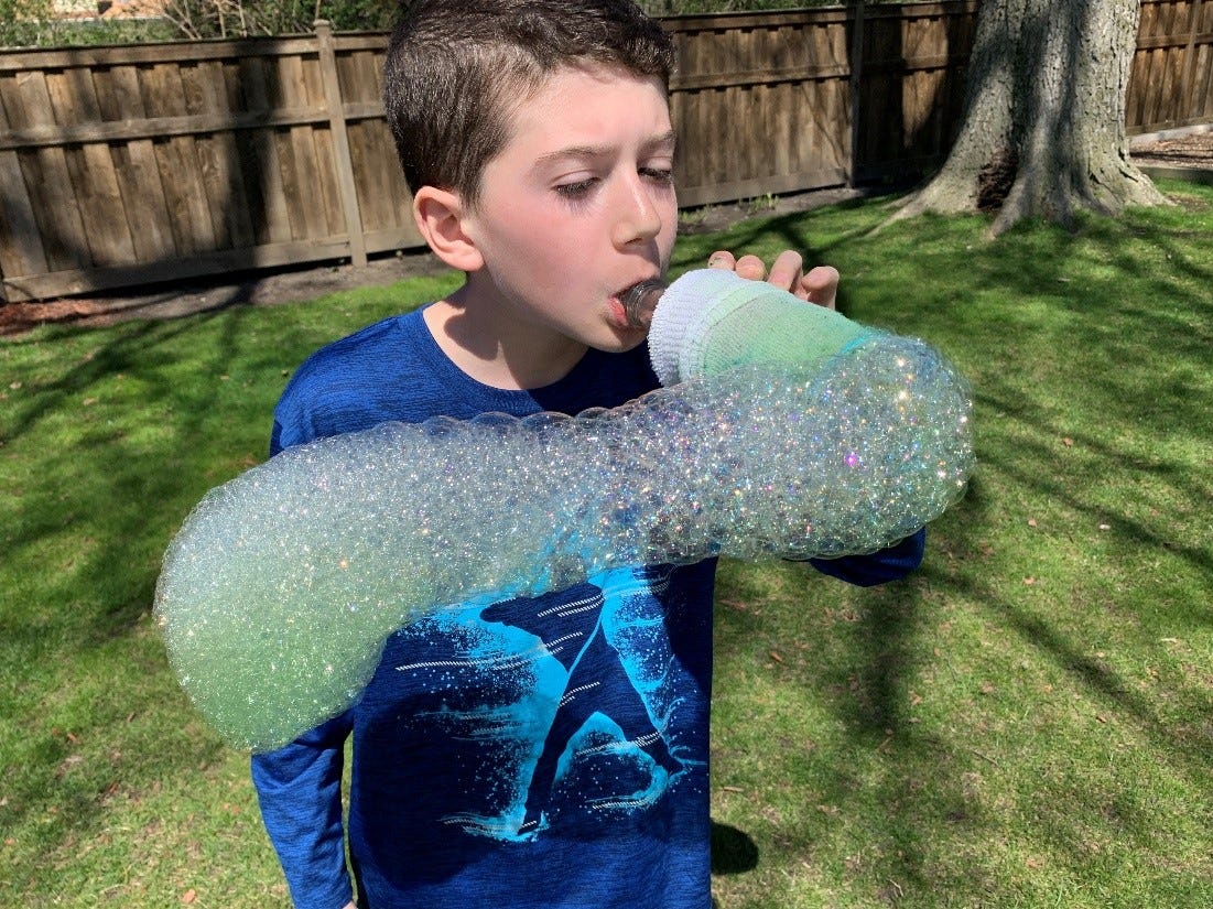 A little boy is seen blowing out a long stream of bubbles that are all attached (first grade science experiments)