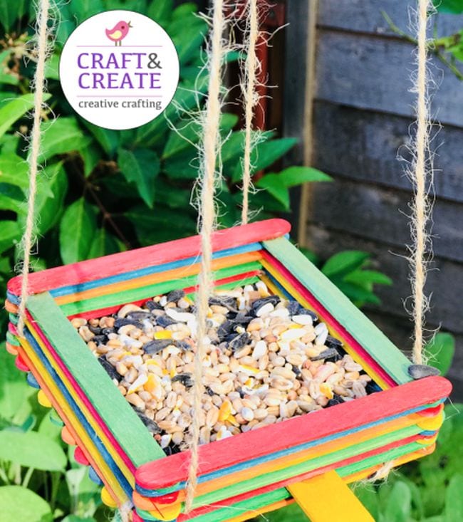 Platform-style bird feeder built from colorful wood craft sticks and filled with mixed seed (First Grade Science Experiments)