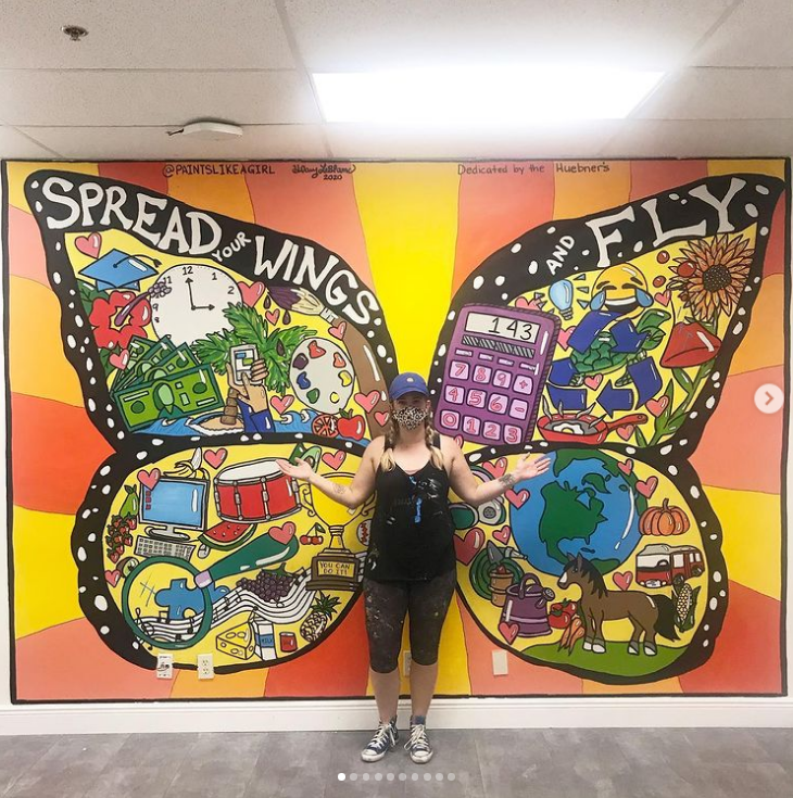 teacher standing in front of a mural of butterfly wings 