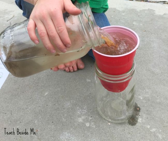 Child pouring dirty water into a cup sitting on top of a large mason jar