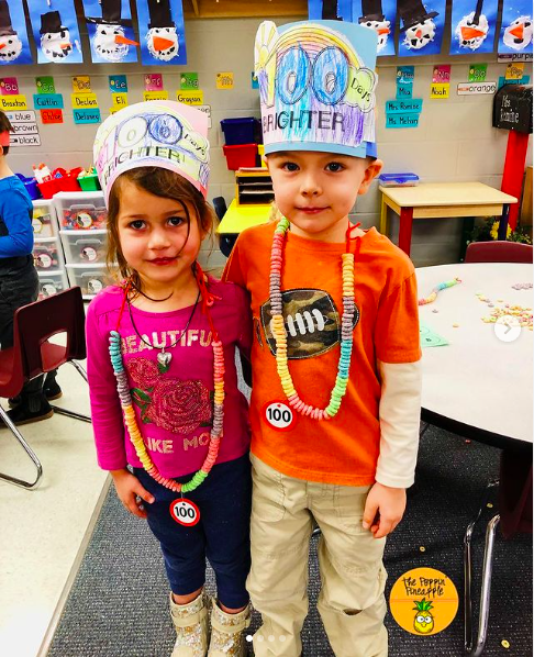 A young boy and girl stand proudly wearing their 100th day Cheerio necklaces and crowns