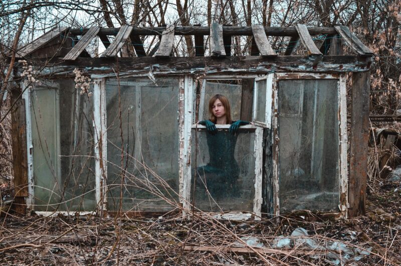 Woman inside an abandoned ramshackle greenhouse in the woods