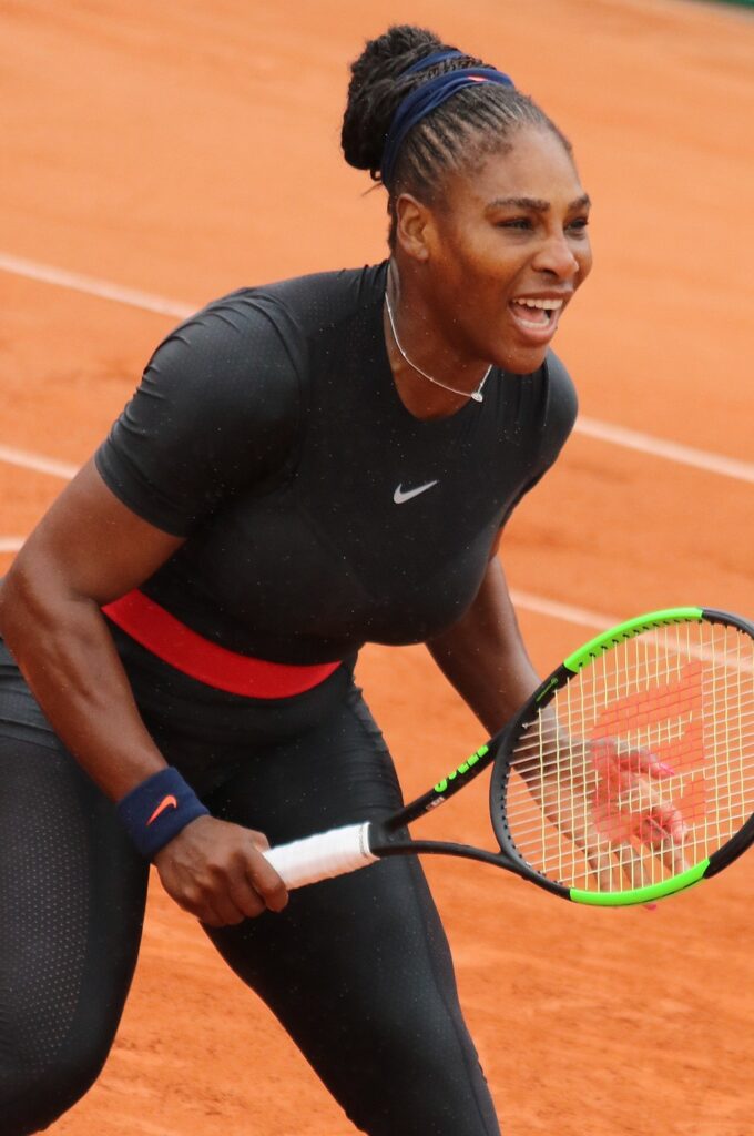 Serena Williams in black bodysuit with red belt on tennis court