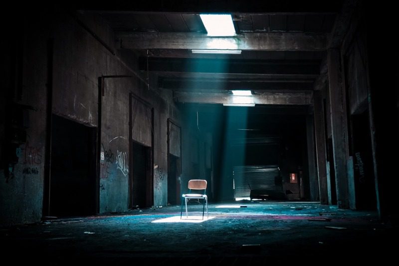 A chair sits in the hallway of an abandoned building under a shaft of light from above (High School Picture Writing Prompts)