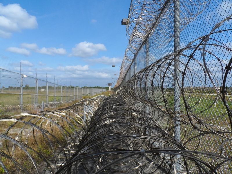 A fence topped by rolls of razor wire against a blue sky