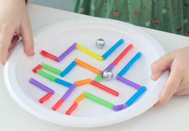 Child holding a marble maze made from straws on a paper plate