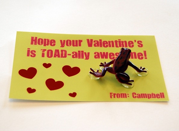 A valentine card with red sticker hearts and a plastic toad attached