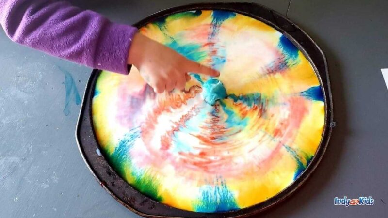 Child's finger pointing to a rainbow swirl experiment