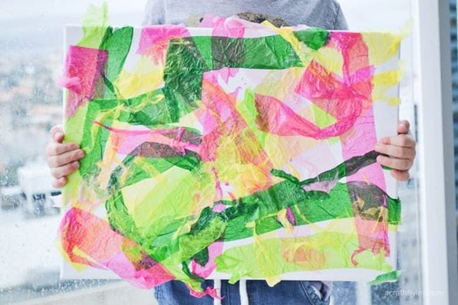 A child is seen holding a large colorful piece of art made from crepe paper in this example of kindergarten art projects.