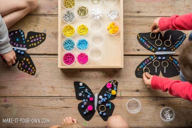 Children's arms and hands are shown making art that looks like butterflies. A palette of paints is also shown in this example of kindergarten art projects.