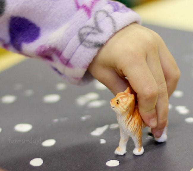 A child's hand is seen holding a small plastic cat.
