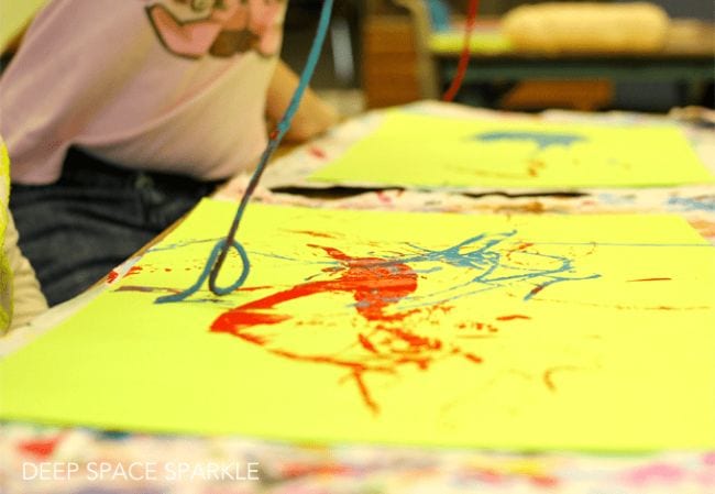 Child dragging a piece of yarn dipped in paint across a piece of yellow paper
