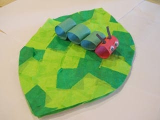 A construction paper caterpillar is seen sitting on a tissue paper leaf.