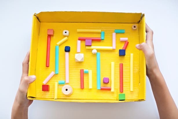 A cardboard box painted yellow is converted into a maze using painted wooden bits