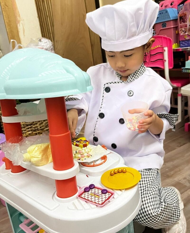 Preschool student dressed as a chef playing in a toy kitchen