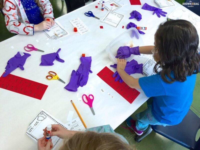Students with purple plastic gloves on cutting apart words and taping them back together with bandaids