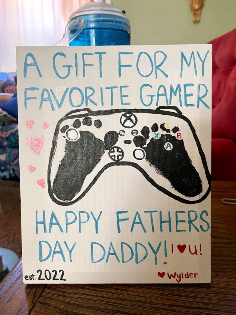 A sign has two black footprints turned into a game controller. Text reads A gift for my favorite gamer. 
