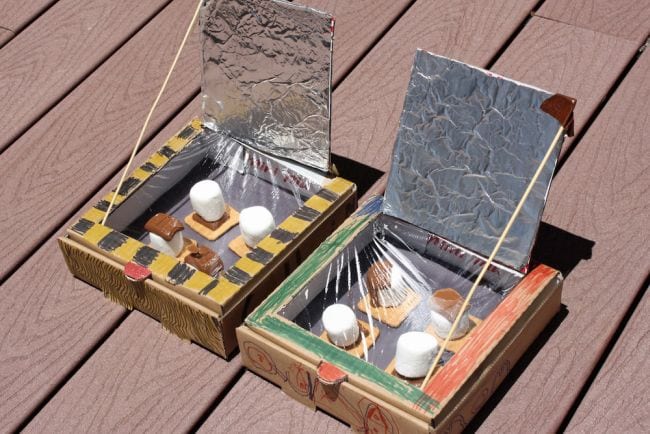 Two pizza boxes turned into solar ovens using foil and other supplies, with marshmallows cooking inside