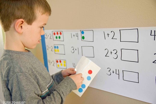 Child using colorful dot stickers to practice addition facts on a wall chart