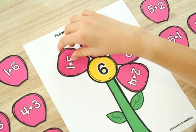 Child gluing petals to a paper flower. The petals have addition facts printed on them, with the matching sum in the middle