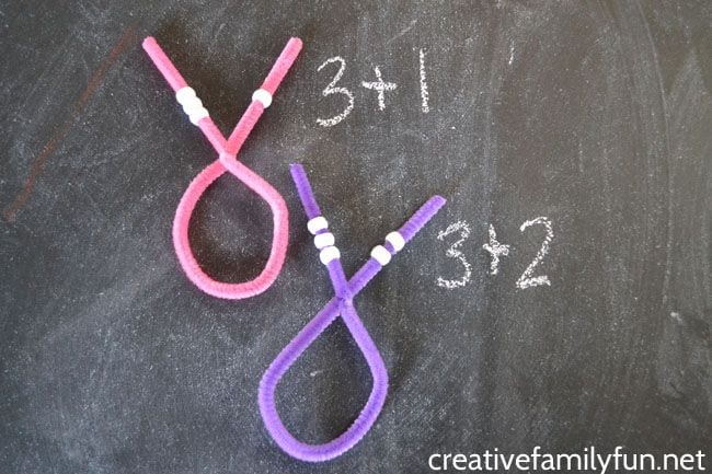 Two pipe cleaners with beads at each ends, twisted into loops, with addition equations written next to them
