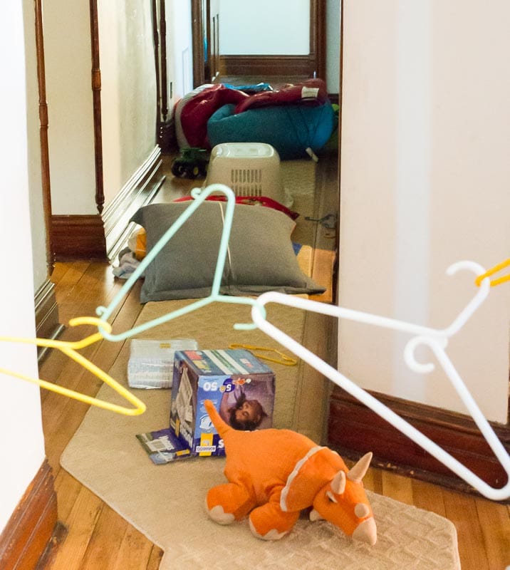Items like a laundry basket, pillow, cardboard box, stuffed dinosaur, and clothes hangers attached to one another are laid out in a path in this example of obstacle courses for kids.