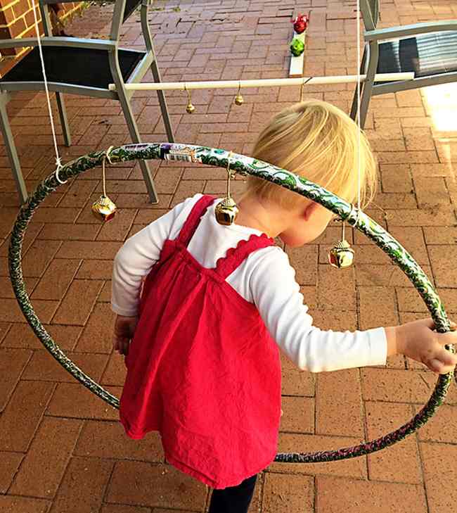 Toddler climbing through a hula hoop with jingle bells attached to it in this example of obstacle courses for kids