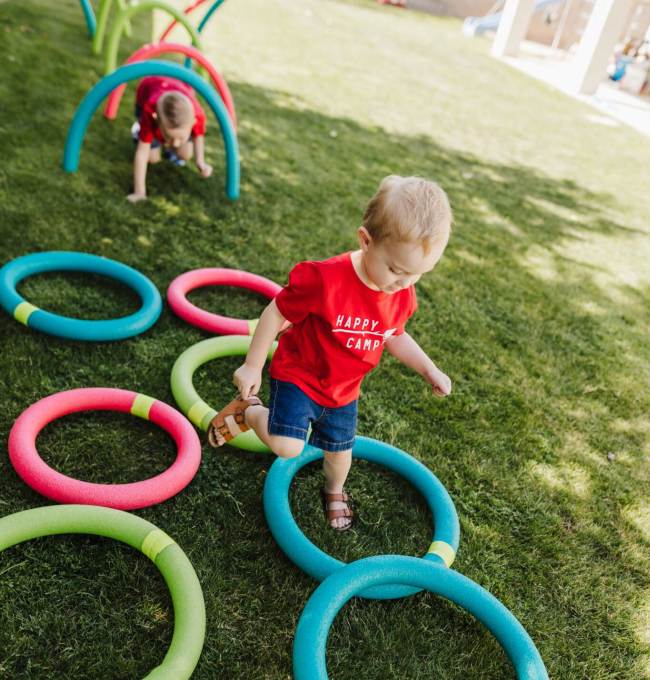 Toddlers climbing under hoops and through circles made of pool noodles in a DIY obstacle course for kids
