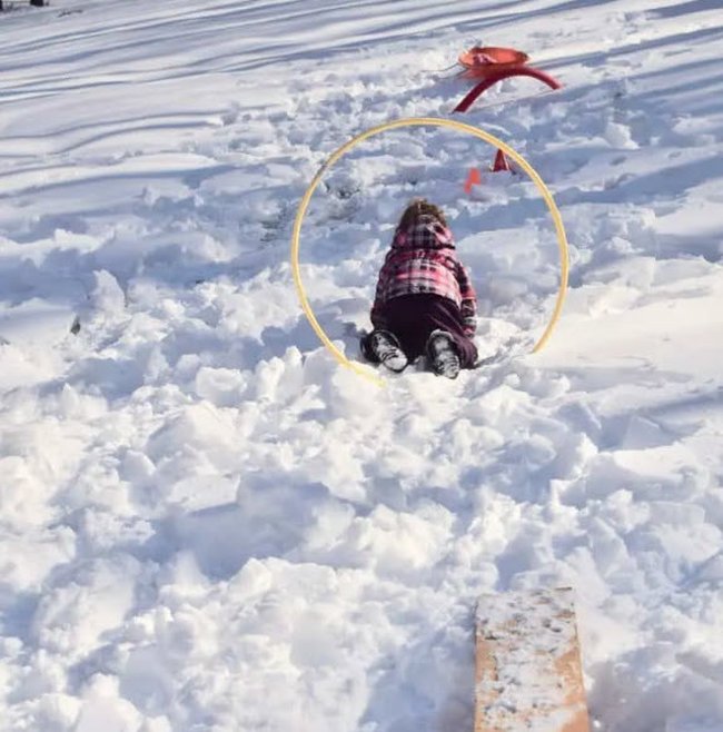 Child climbing through a hoop stuck into a pile or snow in this example of obstacle courses for kids