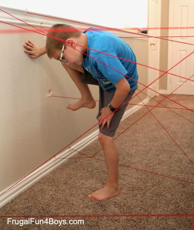 Child climbing over and under strings taped to a wall, trying not to touch them in this example of obstacle courses for kids