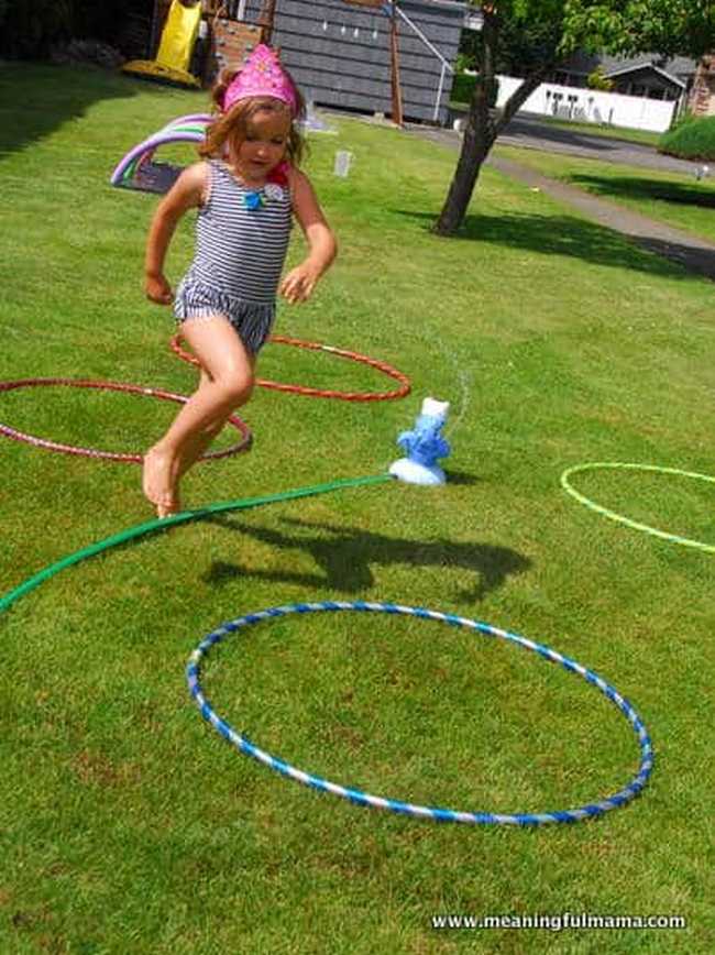 Little girl in a bathing suit running through a backyard obstacle course with sprinklers and other water features in this example of obstacle courses for kids