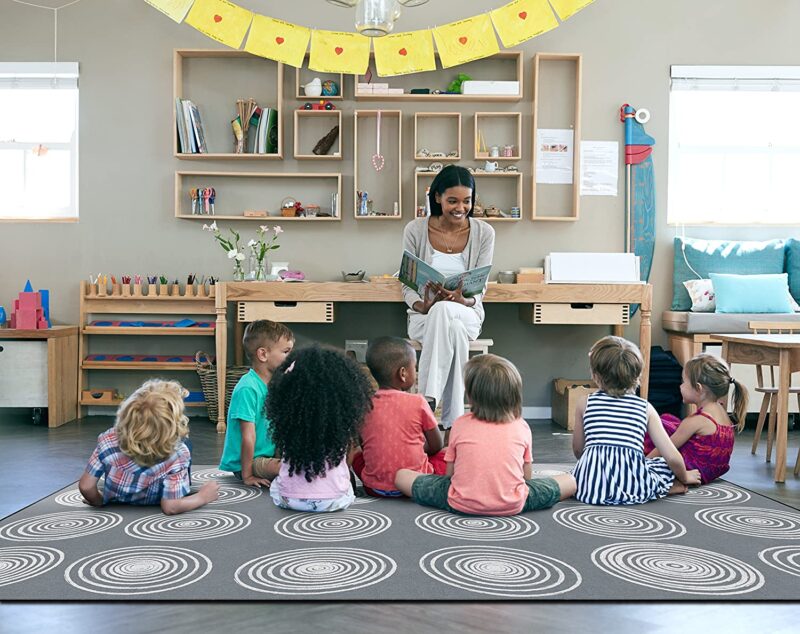 Teacher reading to a classroom of children sitting on a grey rug which is an example of classroom rugs.