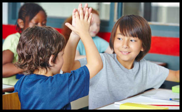 Two boys in classroom exchange high fives.